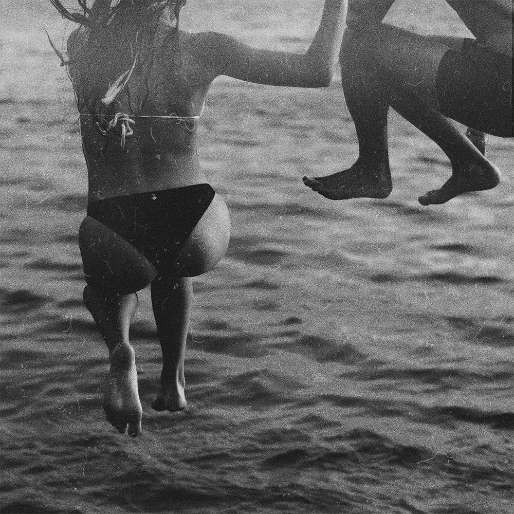 Black & white image of: Two people jumping into a lake. The image is tightly cropped so you can't see their heads or faces. 