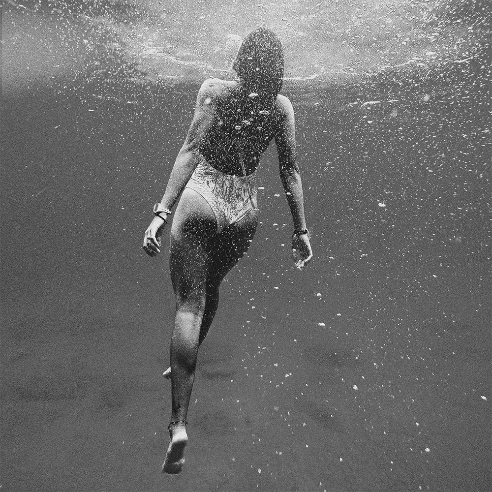 Black & white image of: A woman in a bathing suit, underwater, swimming towards the surface.