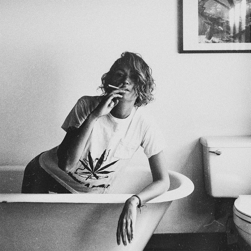 Black & white image of: A woman in a t-shirt and jeans in a bathtub smoking a joint
